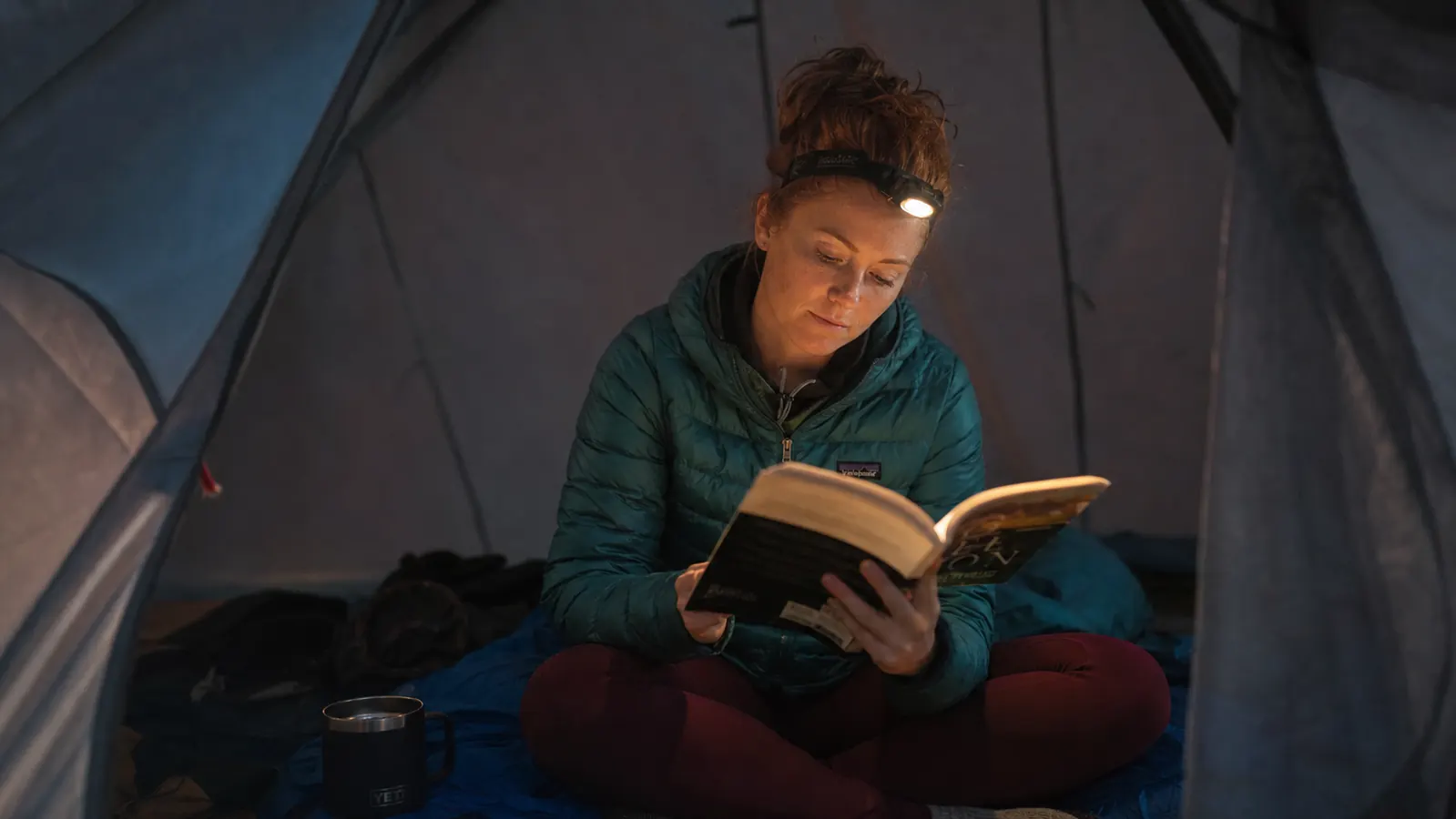 Hiker on a night trail with a bright headlamp beam cutting through darkness in dense forest
